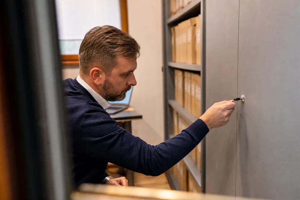 Pracownik działu prawnego zamyka metalową szafę z zamkiem na teczki z dokumentami wierzytelności